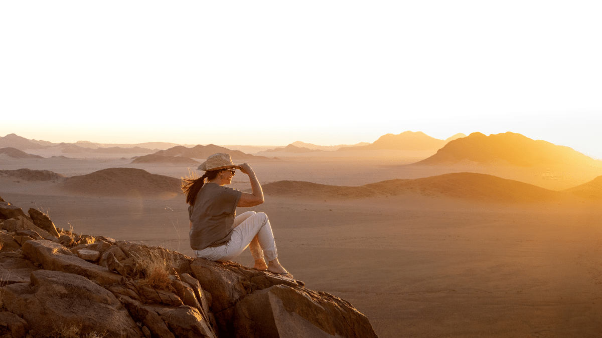 A woman sitting on the top of a mountains at the sunset overview